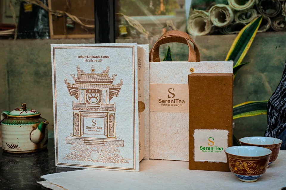 Set sách trà SereniTea đặt cùng túi trà, hộp có quai và chén trà trên bàn